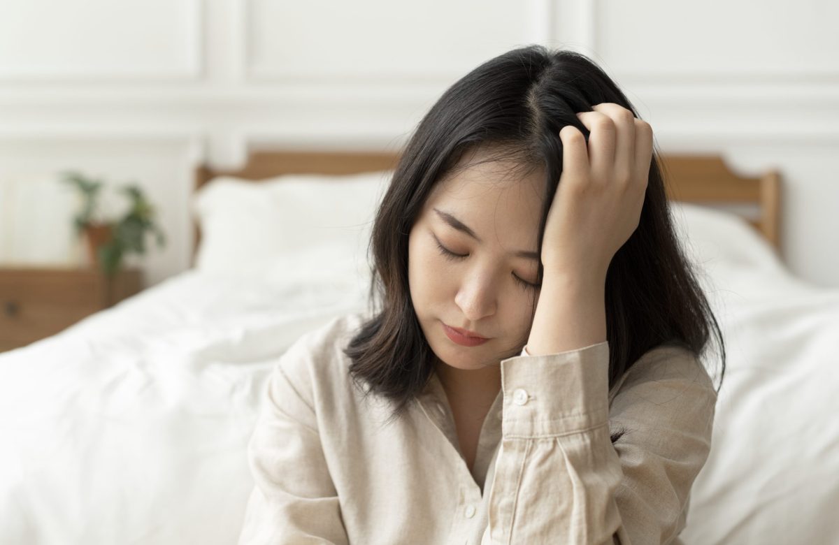 Asian woman sitting sad by her bed